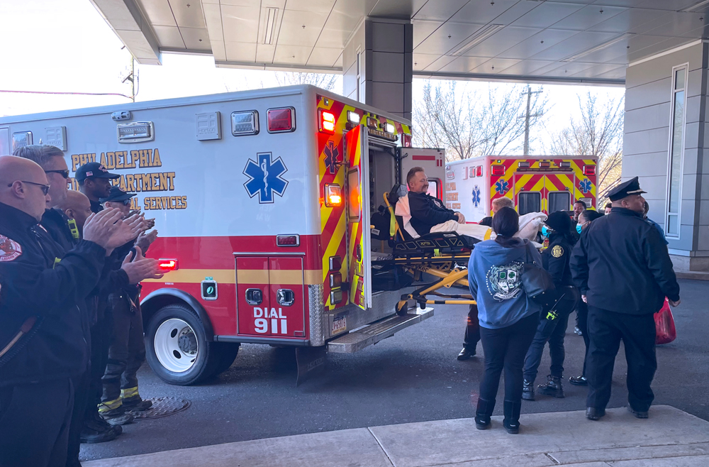 Injured Philadelphia firefighter Randy Ballinger is lifted into an ambulance for transport home, while two lines of first responders clap in support. 
